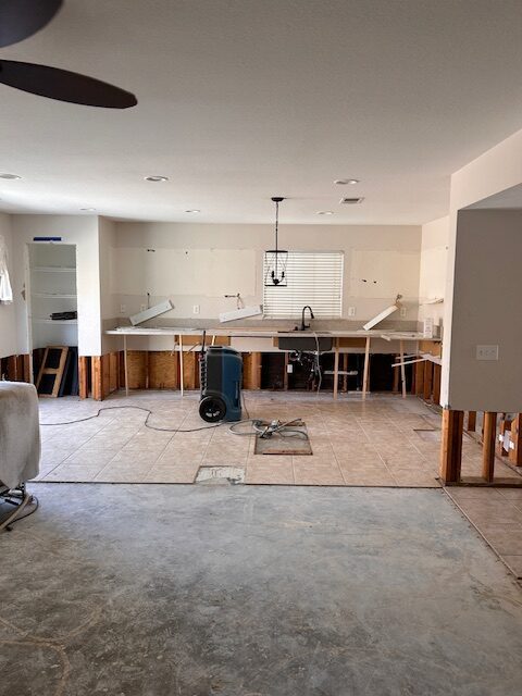 Before photo: kitchen mitigation after water damage with cabinets removed, flood cuts in drywall, and drying equipment on the floor